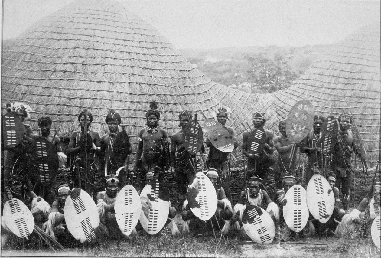 एक झोपड़ी के बाहर ज़ुलु वारियर्स का समूह चित्र, c.1875 (एल्बम प्रिंट) द्वारा अंग्रेजी फोटोग्राफर