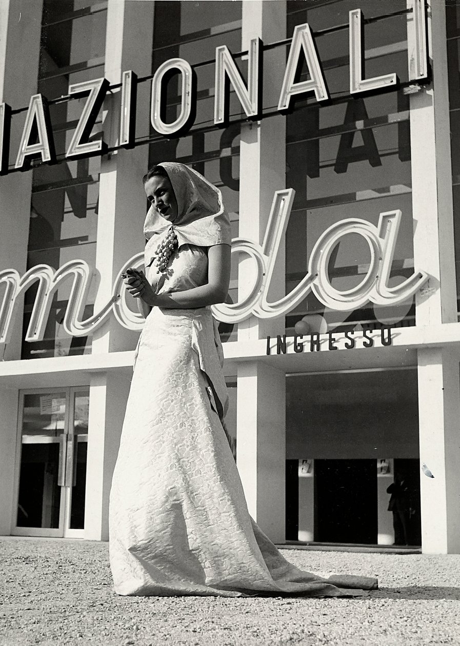 फैशन हाउस "लम्मा" द्वारा बनाए गए वेडिंग गाउन में मॉडल। लेख में मठवासी शैली की एक हेडड्रेस की विशेषता है, जो अंगूर के एक गुच्छा के रूप में एक आकर्षक पिन द्वारा गर्दन पर रखी जाती है। (बी/डब्ल्यू फोटो) द्वारा लुइस बोगिनो