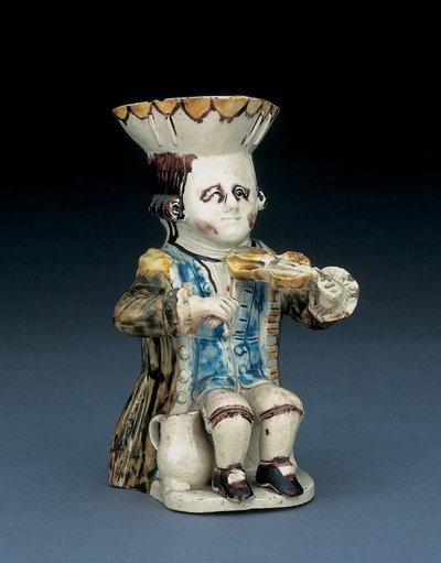 Fiddler toby jug, भूरी और पीली स्कैलप्ड एज वाली उनकी टोपी, उनके भूरे बाल उकेरे हुए और सफ़ेद रोसेट के साथ एक धुले भूरे रंग के फ्रॉक कोट, c.1770 में बंधे हुए थे। द्वारा अंग्रेजी स्कूल